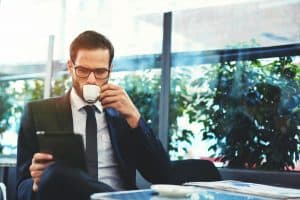 Male small business owner drinking espresso and reading a business book on ipad