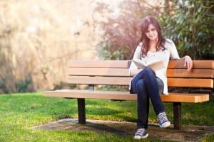 Female entrepreneur reading a book on a park bench.